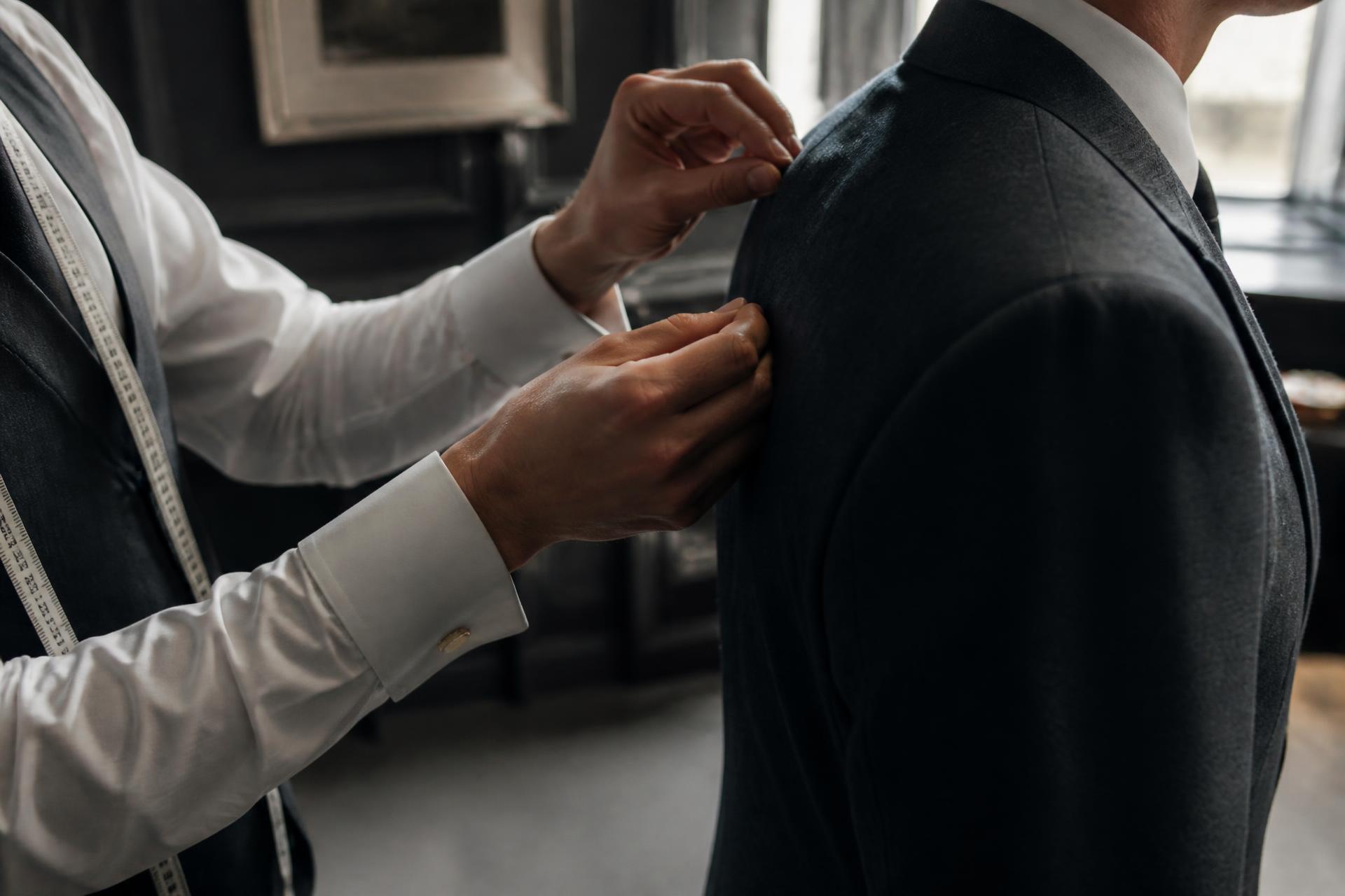 Tailor adjusting the shoulder of a charcoal wool jacket during a private fitting