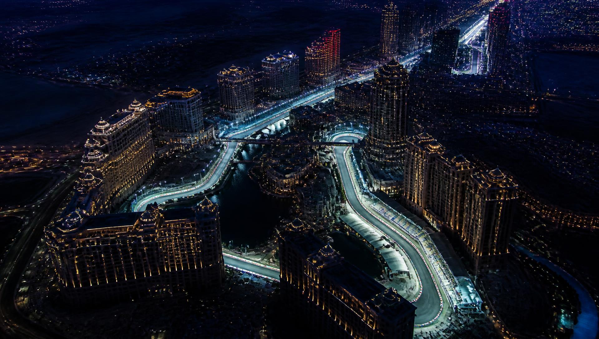 Aerial night view of a floodlit street circuit threading between illuminated resort towers