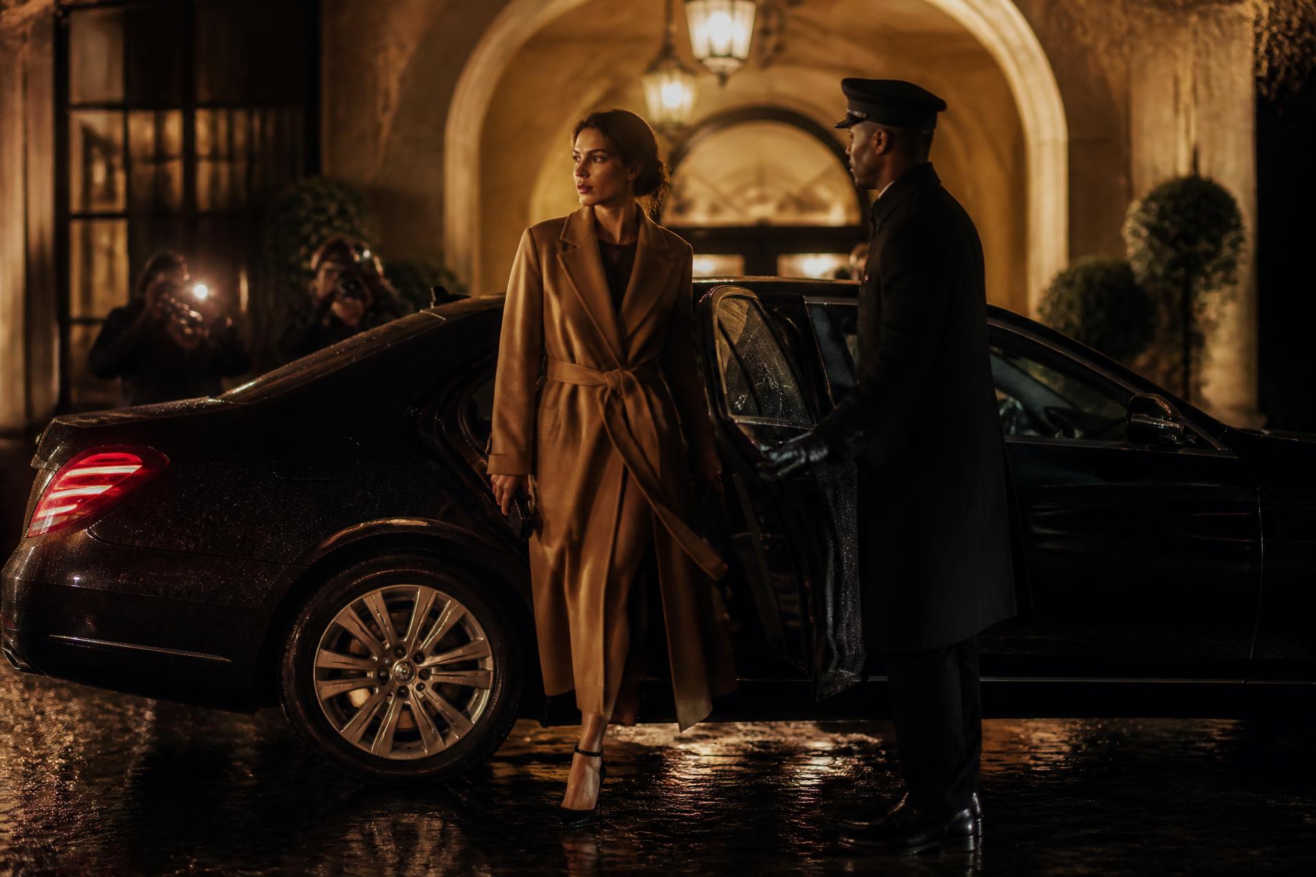 Guest in a camel coat stepping from a black chauffeured car outside a lit Milanese palazzo entrance at night