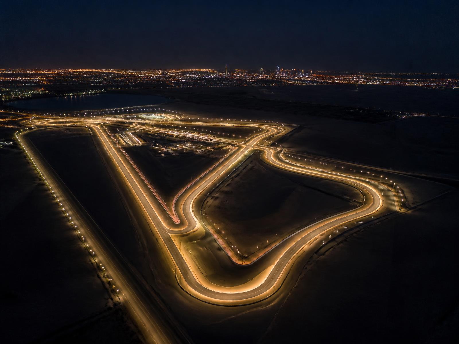 Aerial night view of a floodlit desert racing circuit glowing in darkness