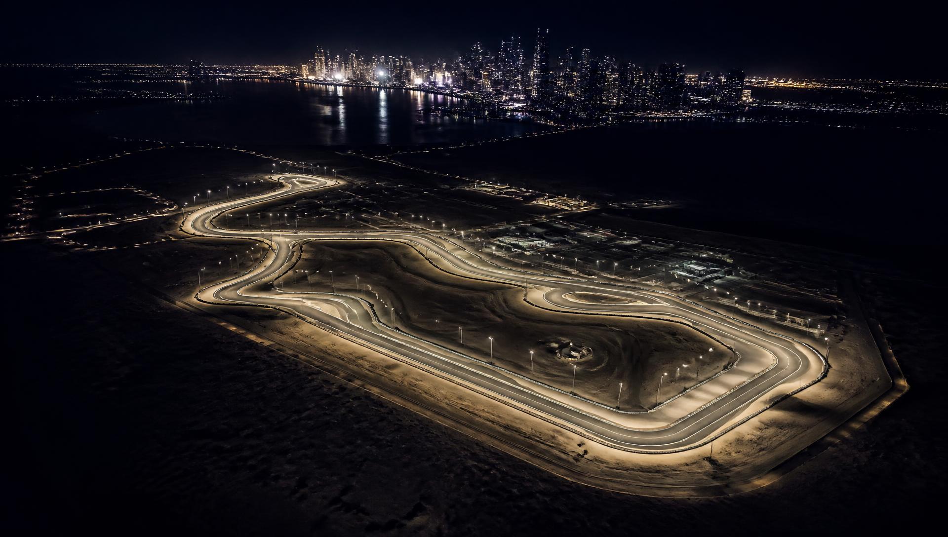 Aerial night view of an illuminated desert racing circuit with a distant Gulf skyline