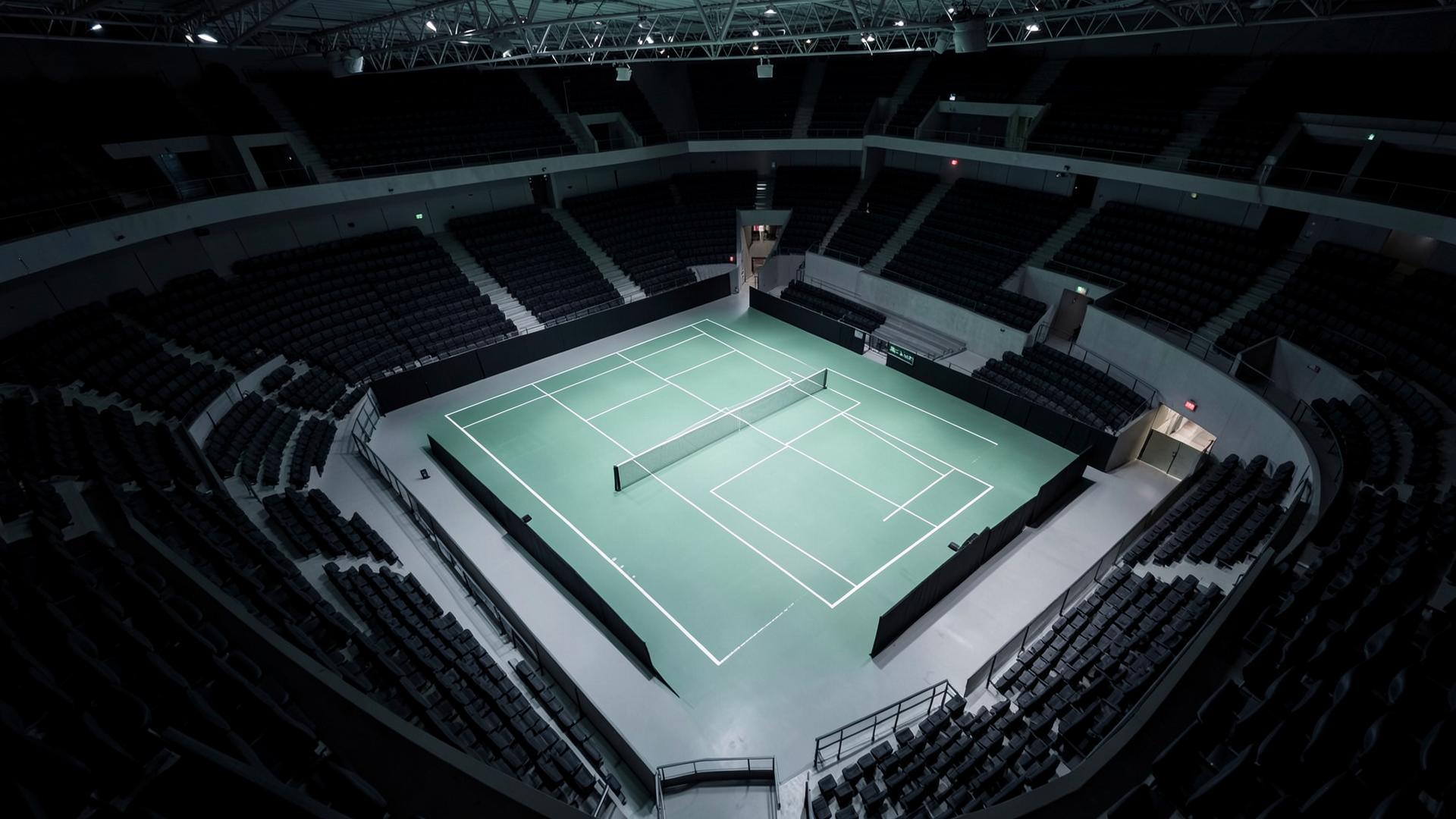 High angle view of an illuminated indoor tennis court from the upper tier of a modern arena
