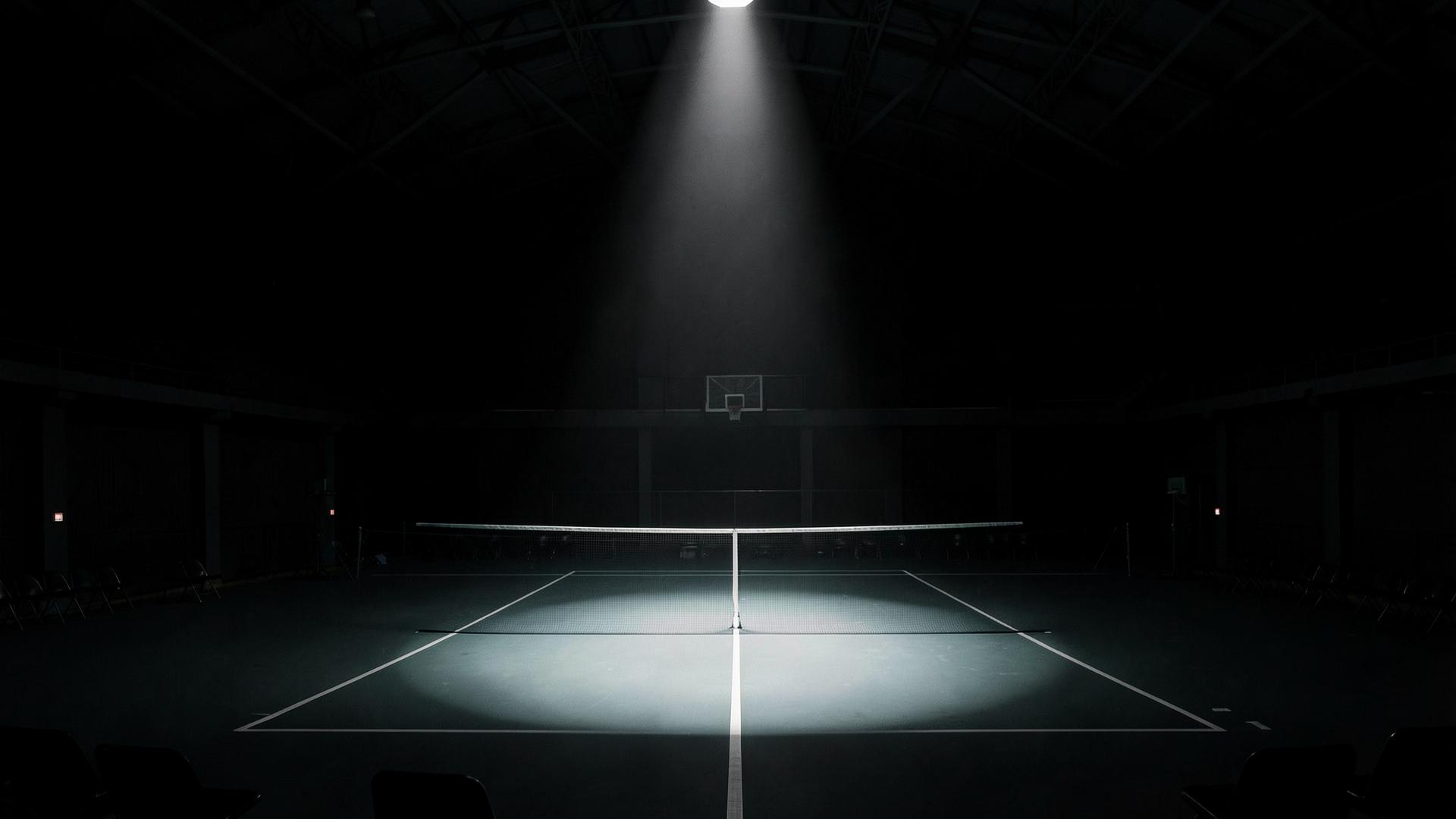 Empty illuminated indoor tennis court under a single spotlight in a dark arena